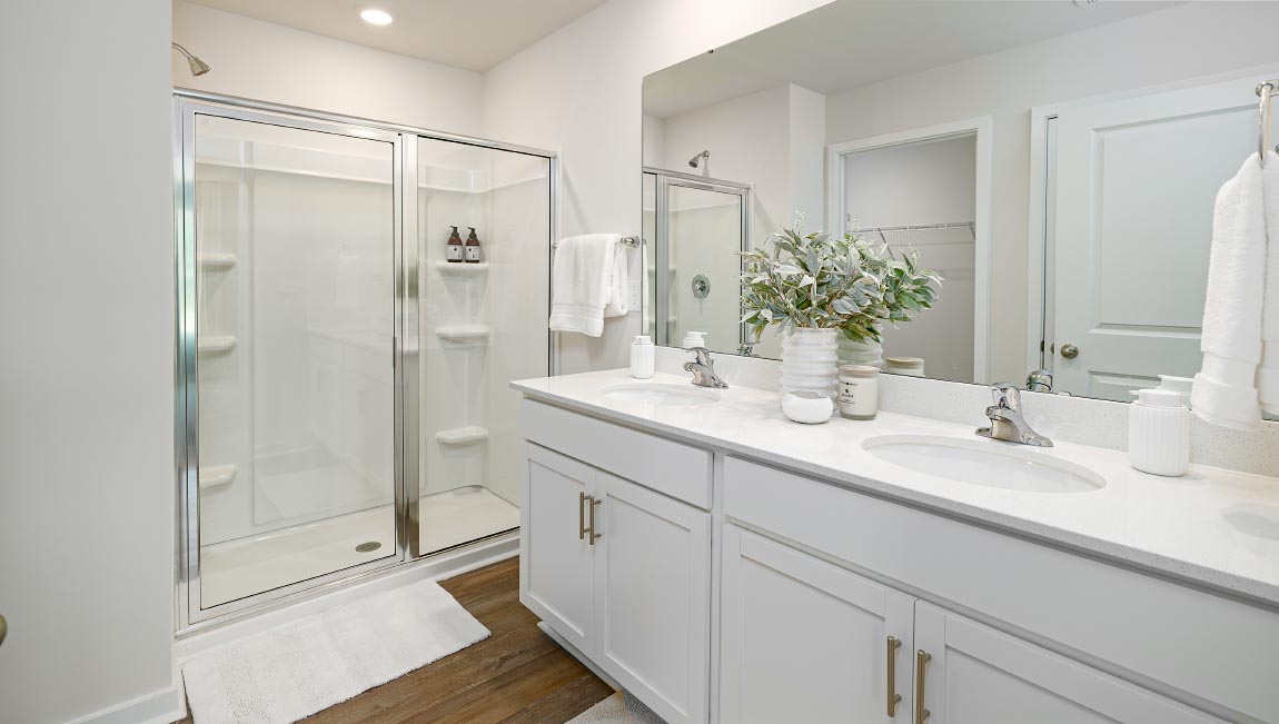 Bathroom with double sink vanity, white counters and cabinets, standing glass door shower