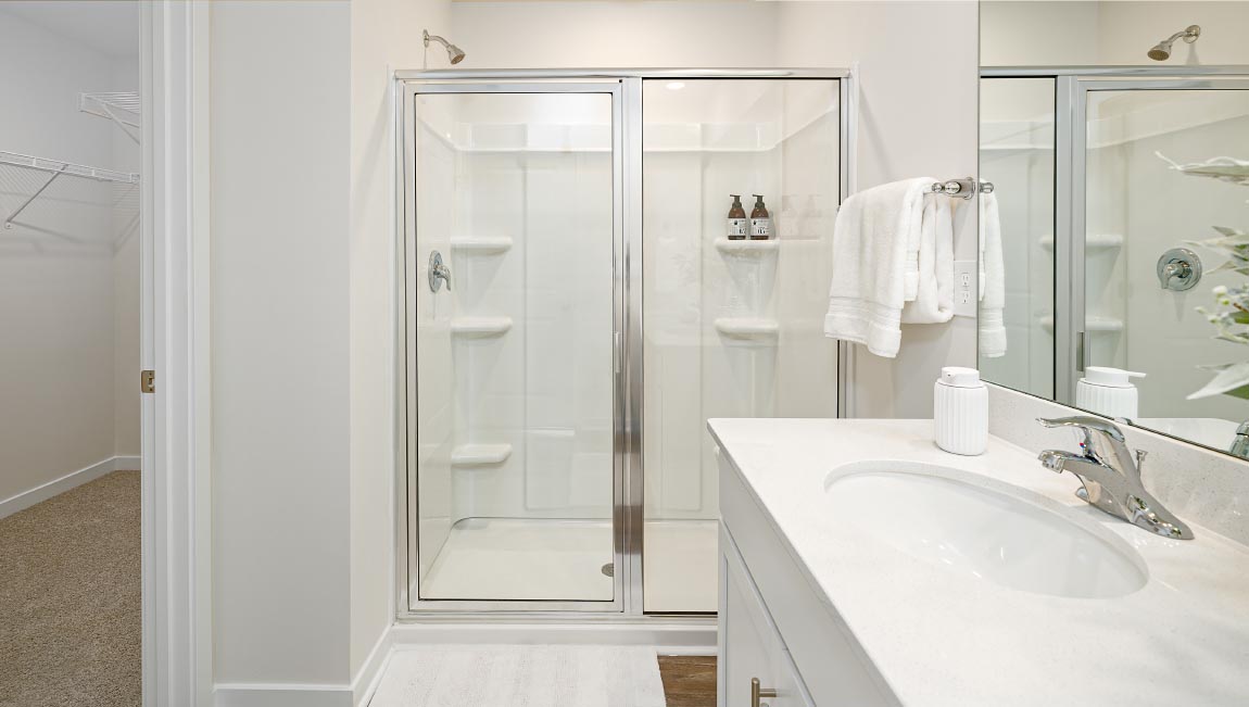 Bathroom with double sink vanity, white counters and cabinets, standing glass door shower