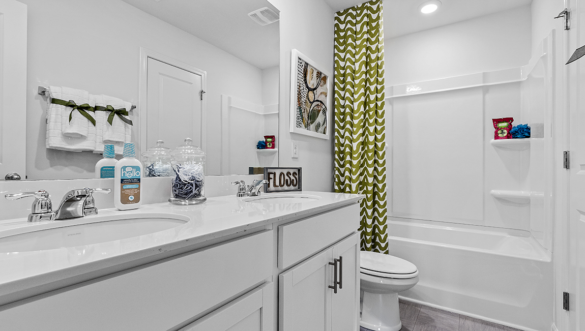 Bathroom with double sinks, bathtub, and white cabinets and counters