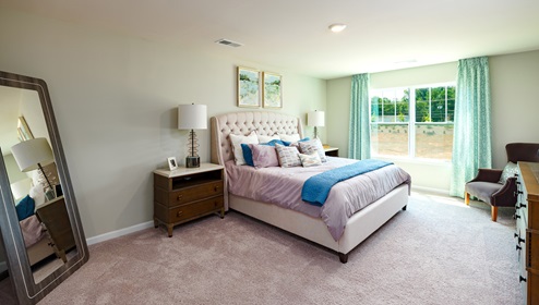 Model primary carpeted bedroom with large window