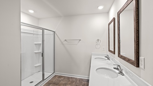 primary bathroom with white counters and cabinets, glass door shower, and tile floors