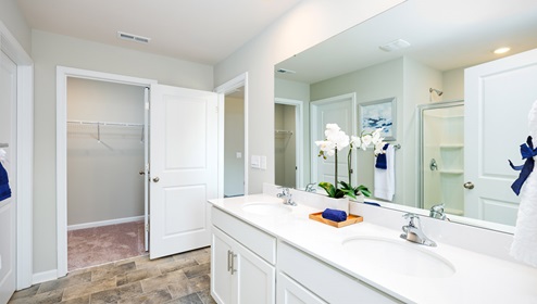 Model primary bathroom with white cabinets and counters, double sinks, and glass door shower