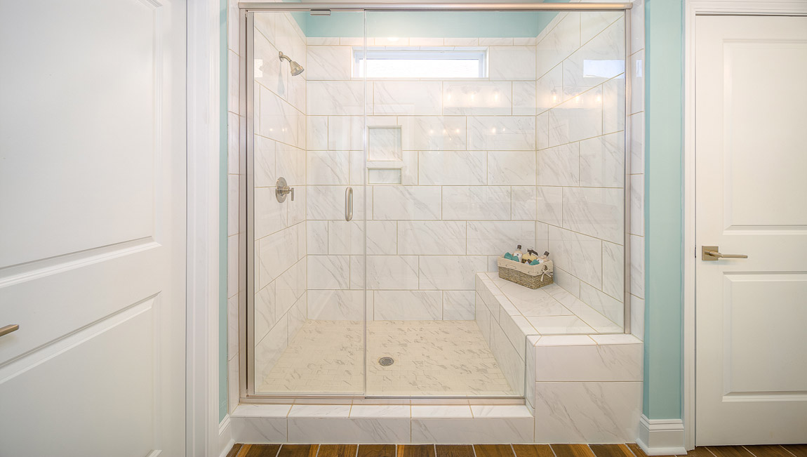 Primary bathroom with white cabinets, double sinks, and glass door shower