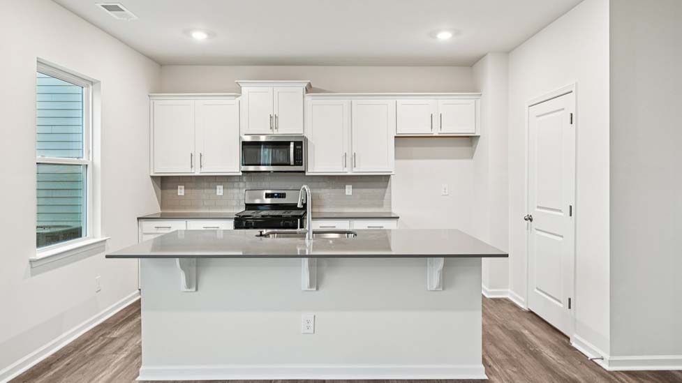 Kitchen and island with white cabinets and counters, vinyl floors and stainless steel appliances