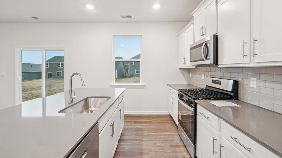 Kitchen and island with white cabinets and counters, vinyl floors and stainless steel appliances