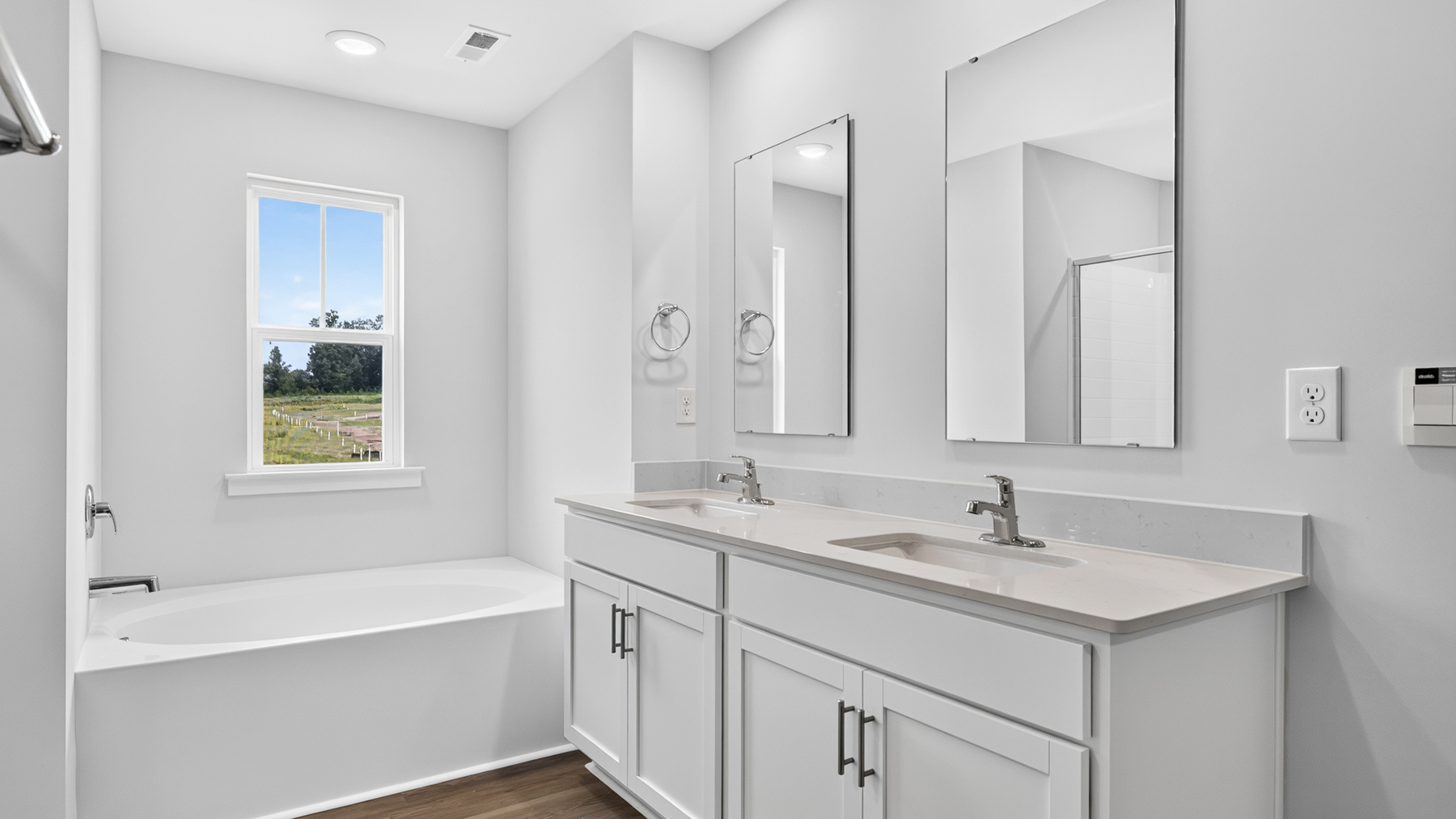 Model primary bathroom with white cabinets and counters, double sinks, and glass door shower