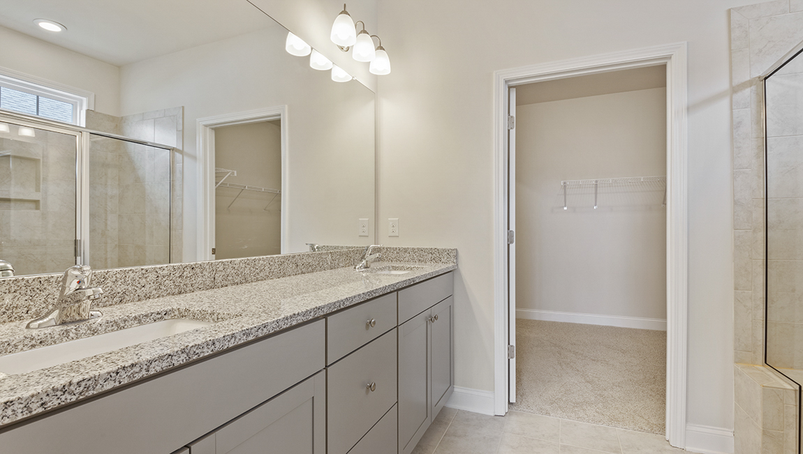 Primary bathroom with white cabinets and counters, view of closet