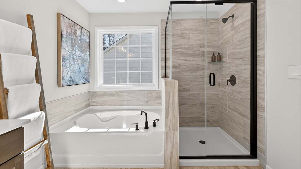 Primary bathroom with double sinks, brown cabinets and bathtub and glass door shower combination