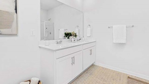 Bathroom with double sinks, white cabinets and counters, and wood floors