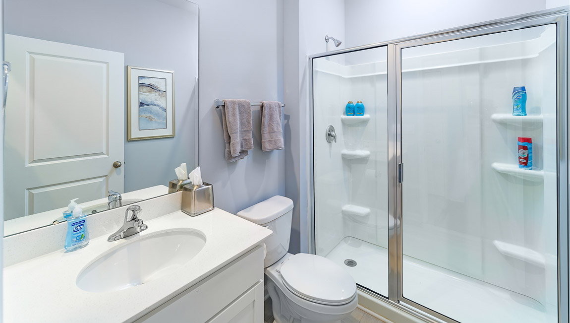 Model bathroom with white counters and cabinets, double sinks and glass door shower