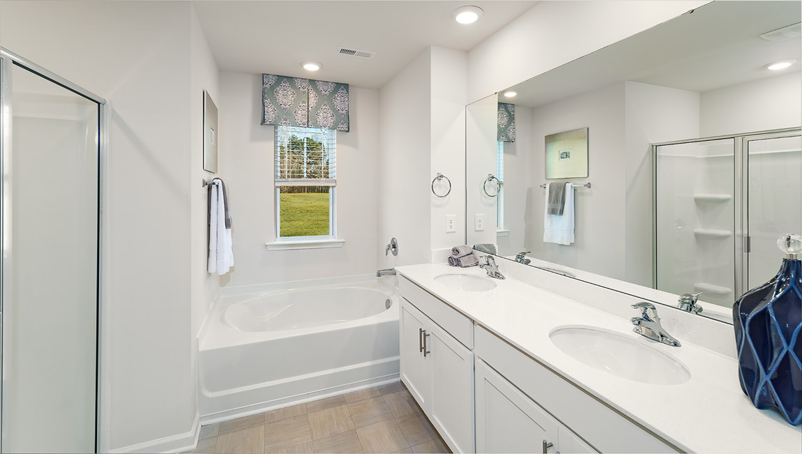 Model primary bathroom with white cabinets and counters, double sinks, and glass door shower