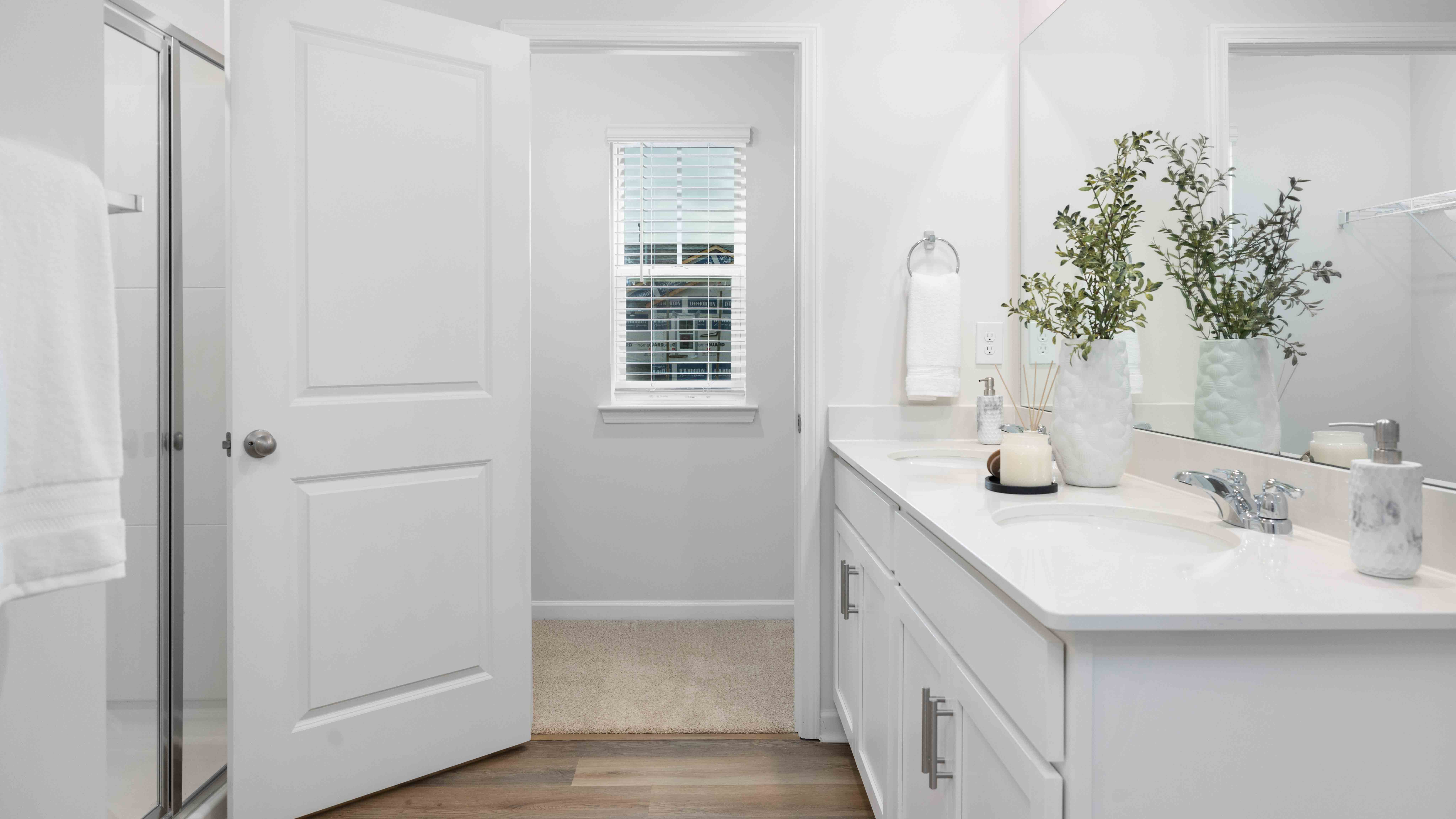 Model bathroom with white counters and cabinets, double sinks and glass door shower