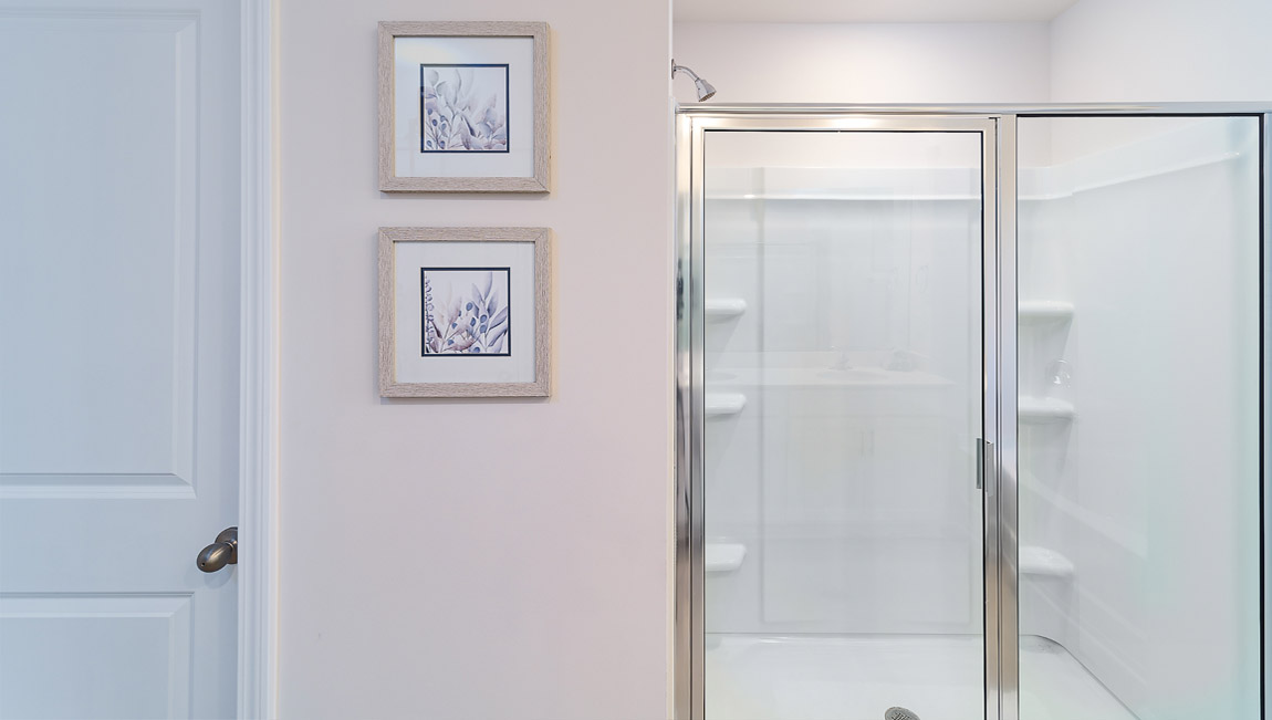 Model bathroom with white counters and cabinets, double sinks and glass door shower