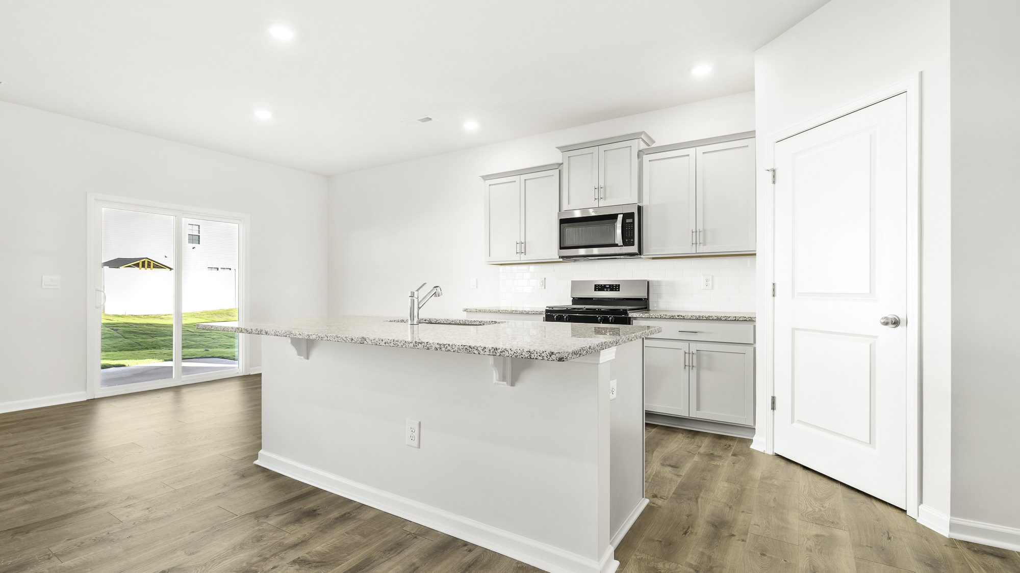 Kitchen featuring a stone-topped island with an integrated sink, wood-finish flooring, light-colored cabinetry, stainless steel appliances, and sliding glass doors