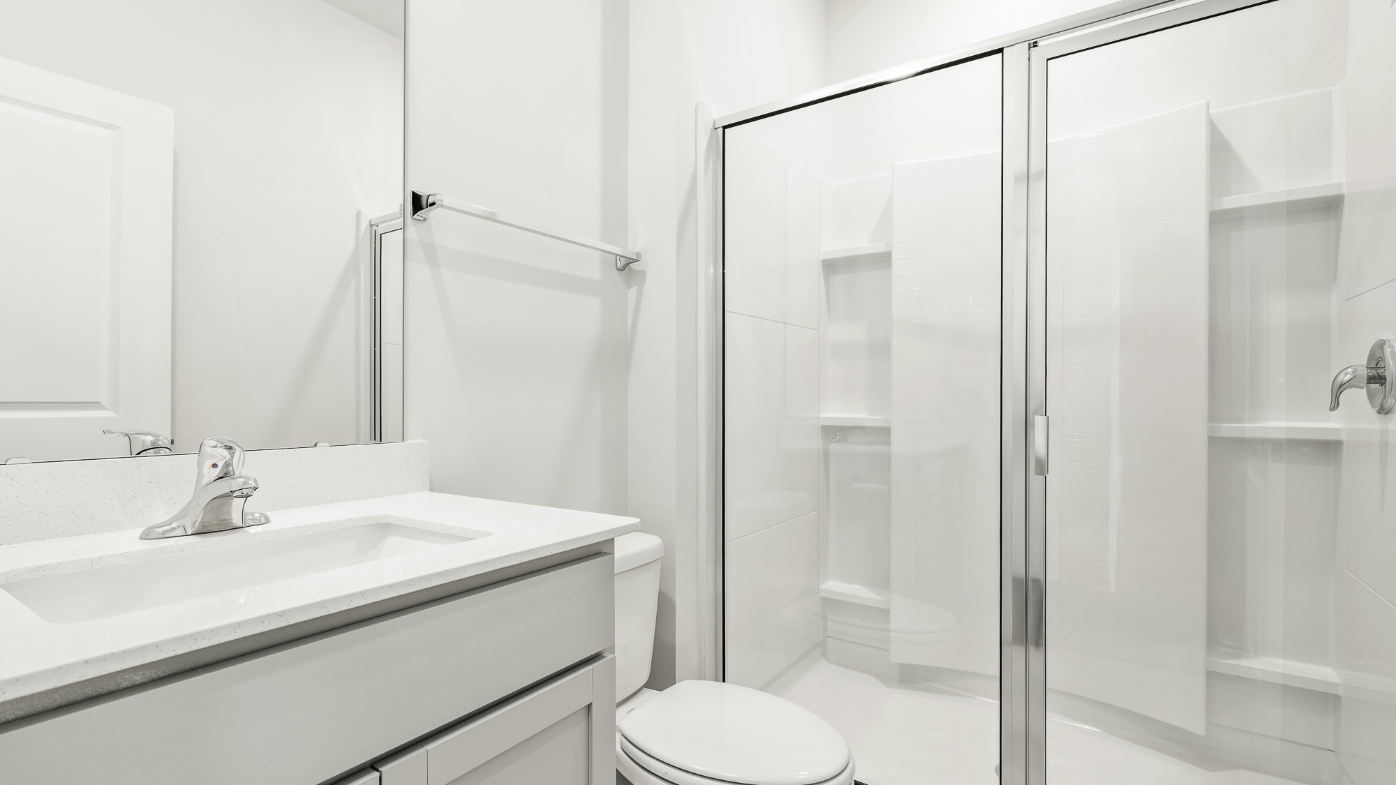 Bathroom featuring a vanity with a white countertop and integrated sink, a large wall-mounted mirror, and a walk-in shower with glass enclosure and built-in shelving