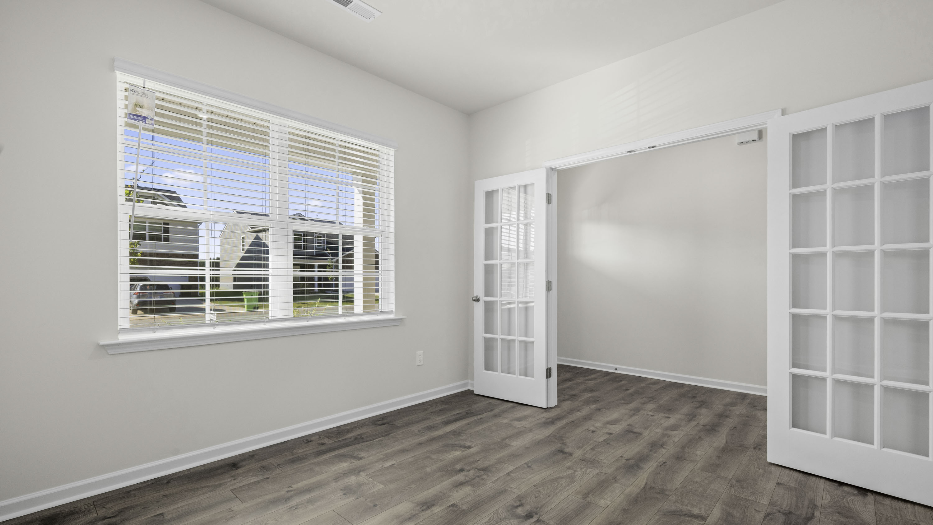 Room featuring wood-finish flooring, white walls, large window with blinds, and white French doors