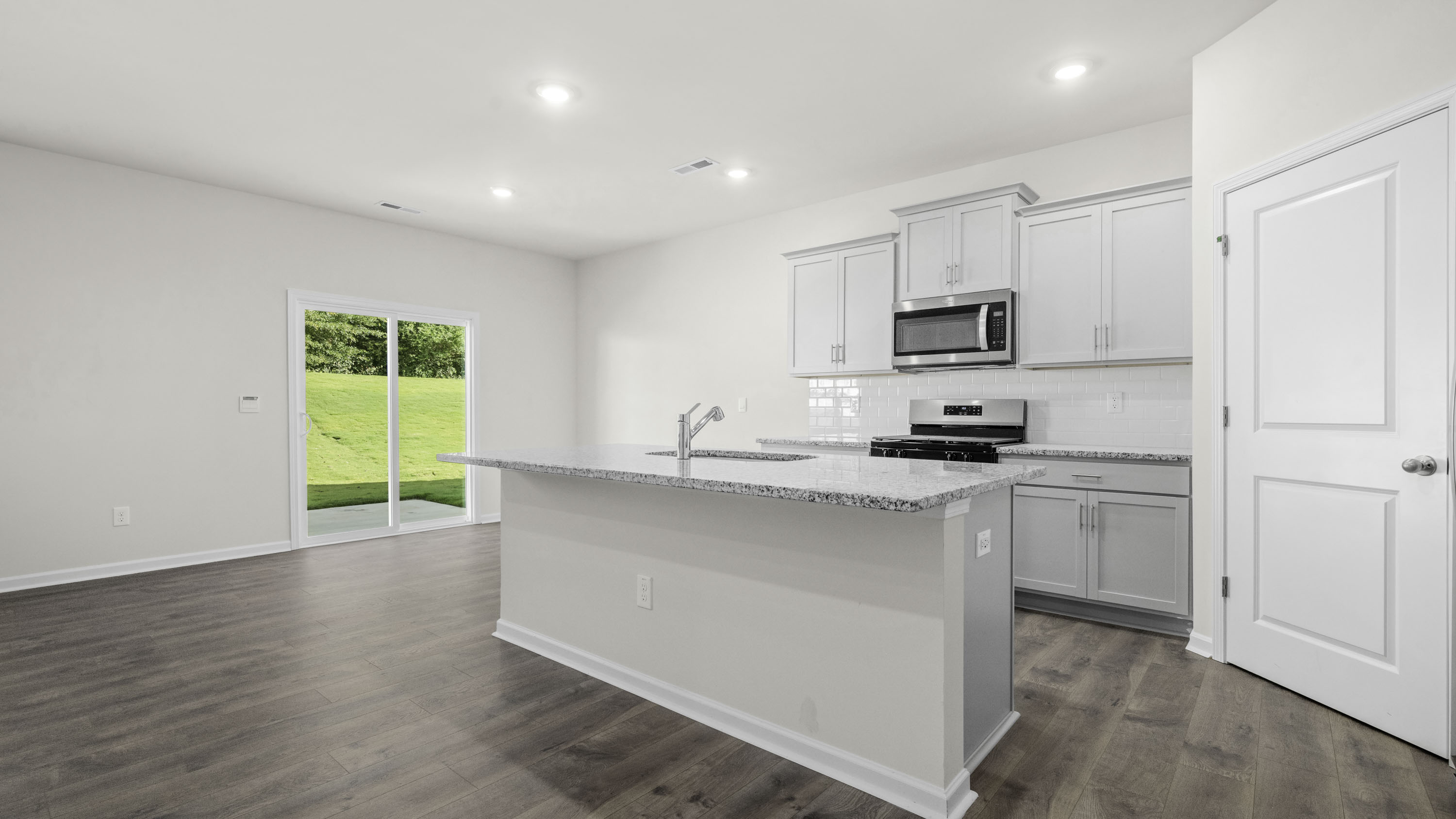 Kitchen featuring light-toned cabinetry, stone-finish countertops, a center island with a stainless steel sink, wood-finish flooring, and sliding glass doors
