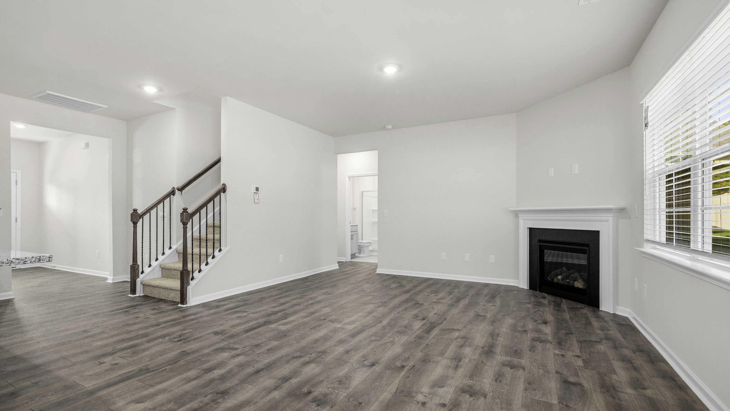 Living area featuring wood-finish flooring, a corner fireplace with a white mantel, recessed lighting, and a staircase with a wooden handrail