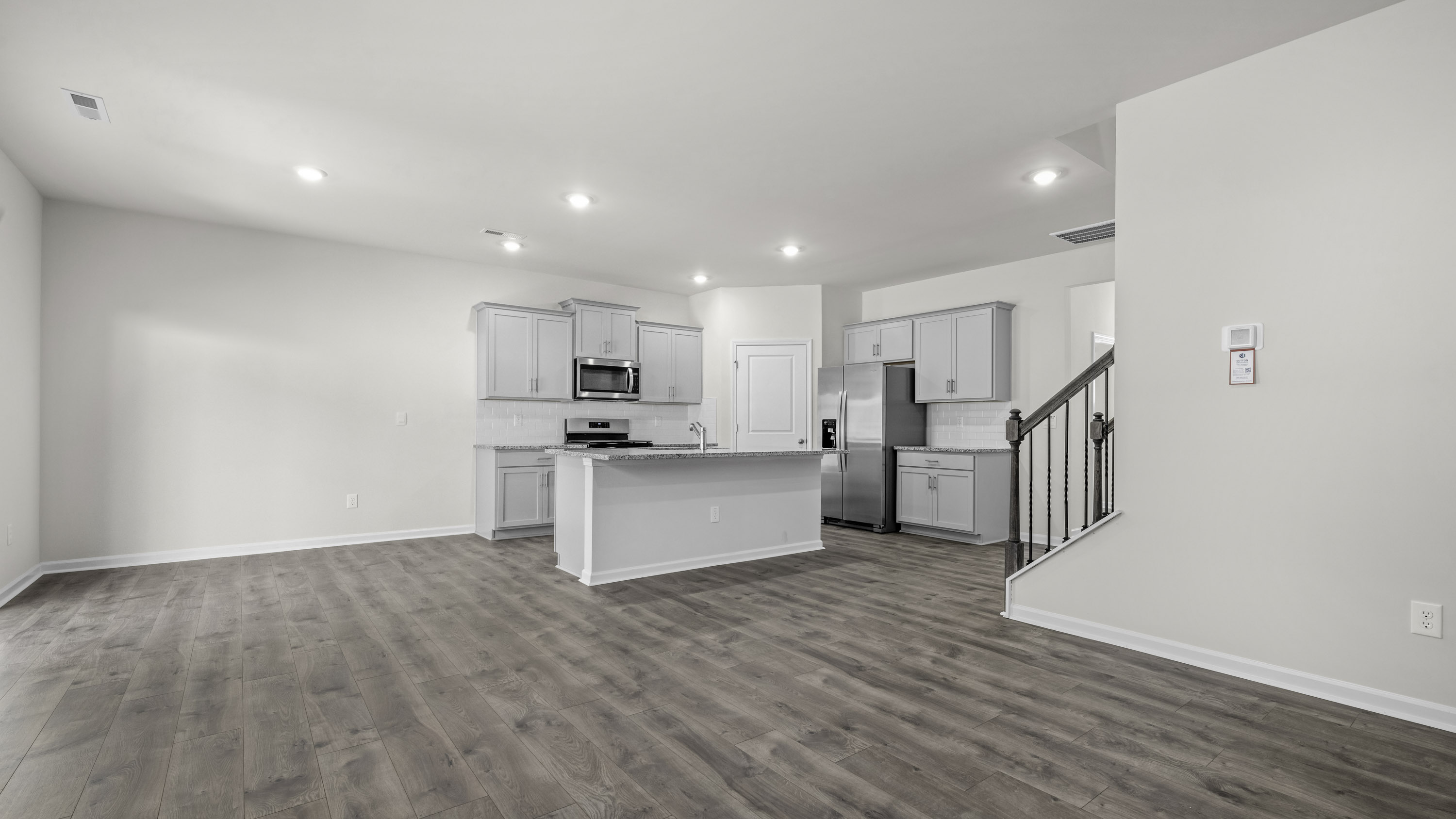 Kitchen featuring light grey cabinetry, stone-finish countertops, stainless steel appliances, an island, and wood-finish flooring