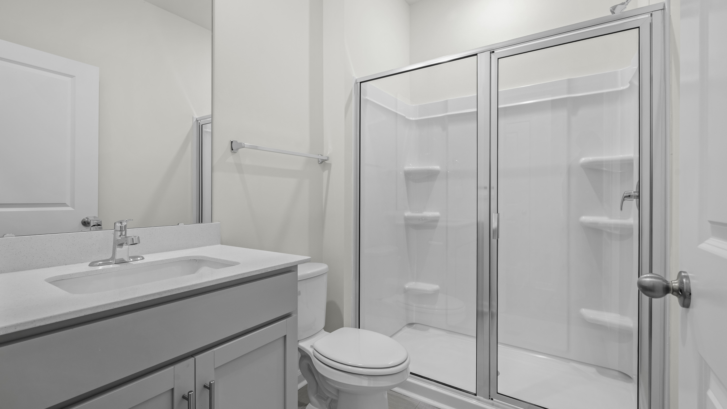 Bathroom featuring a vanity with a white countertop and integrated sink, a glass-enclosed shower with a molded surround, a toilet, and a wall-mounted mirror