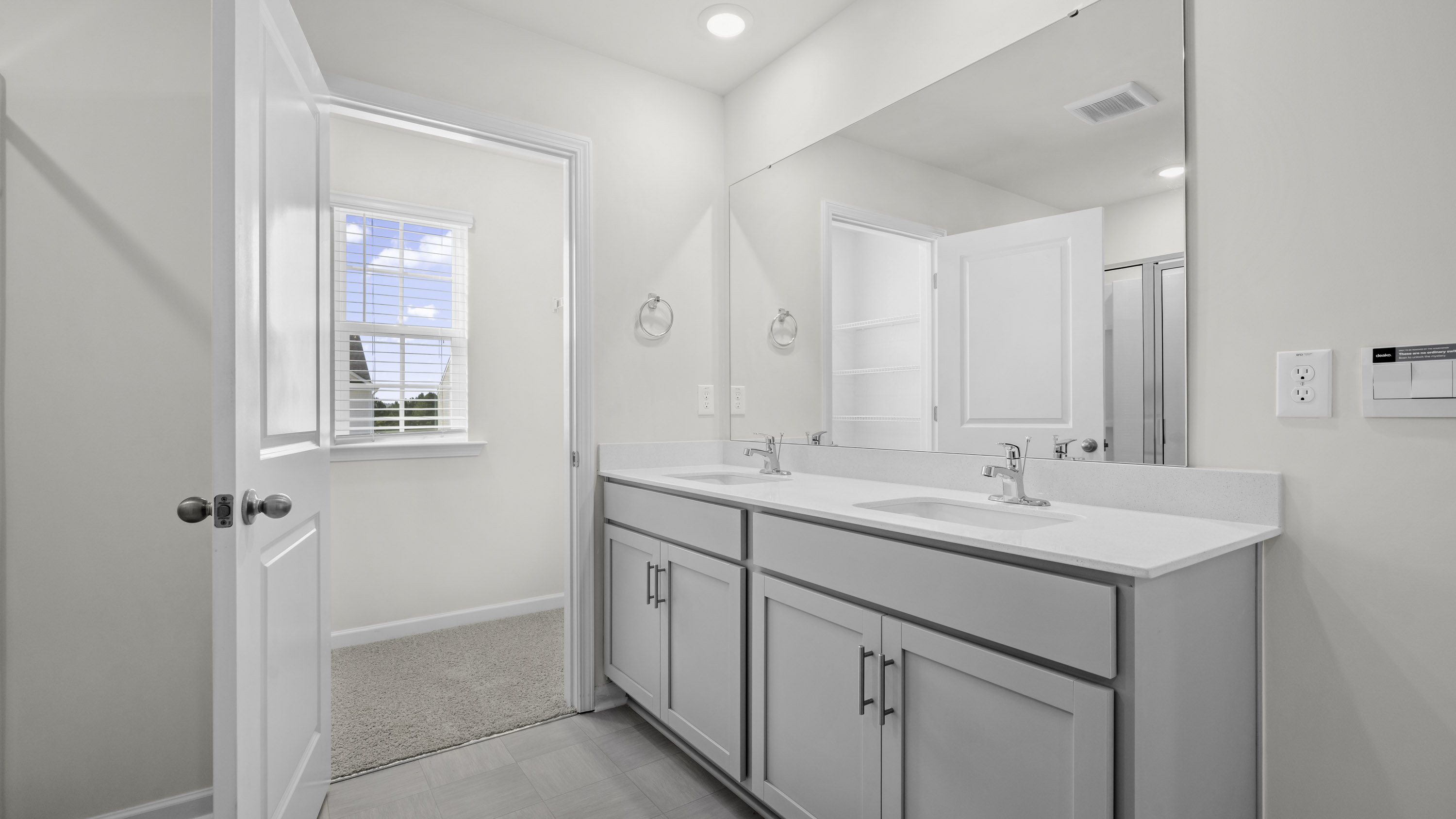 Bathroom featuring a dual-sink vanity with light-toned cabinetry, quartz countertop, polished chrome fixtures, and a large-format vanity mirror