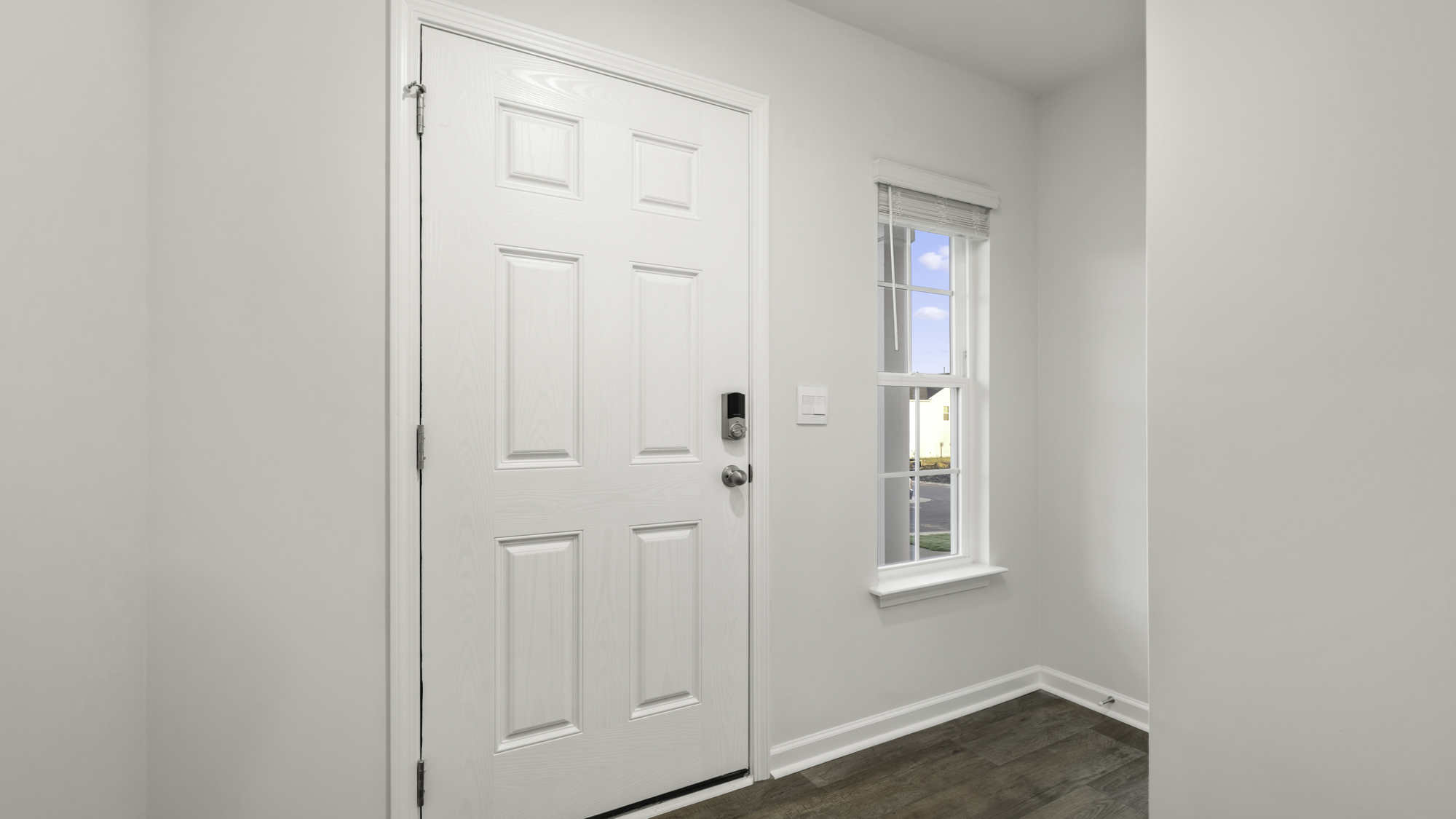 Six-panel white entry door with smart lock technology, wood-finish flooring, and a single-hung window with muntins