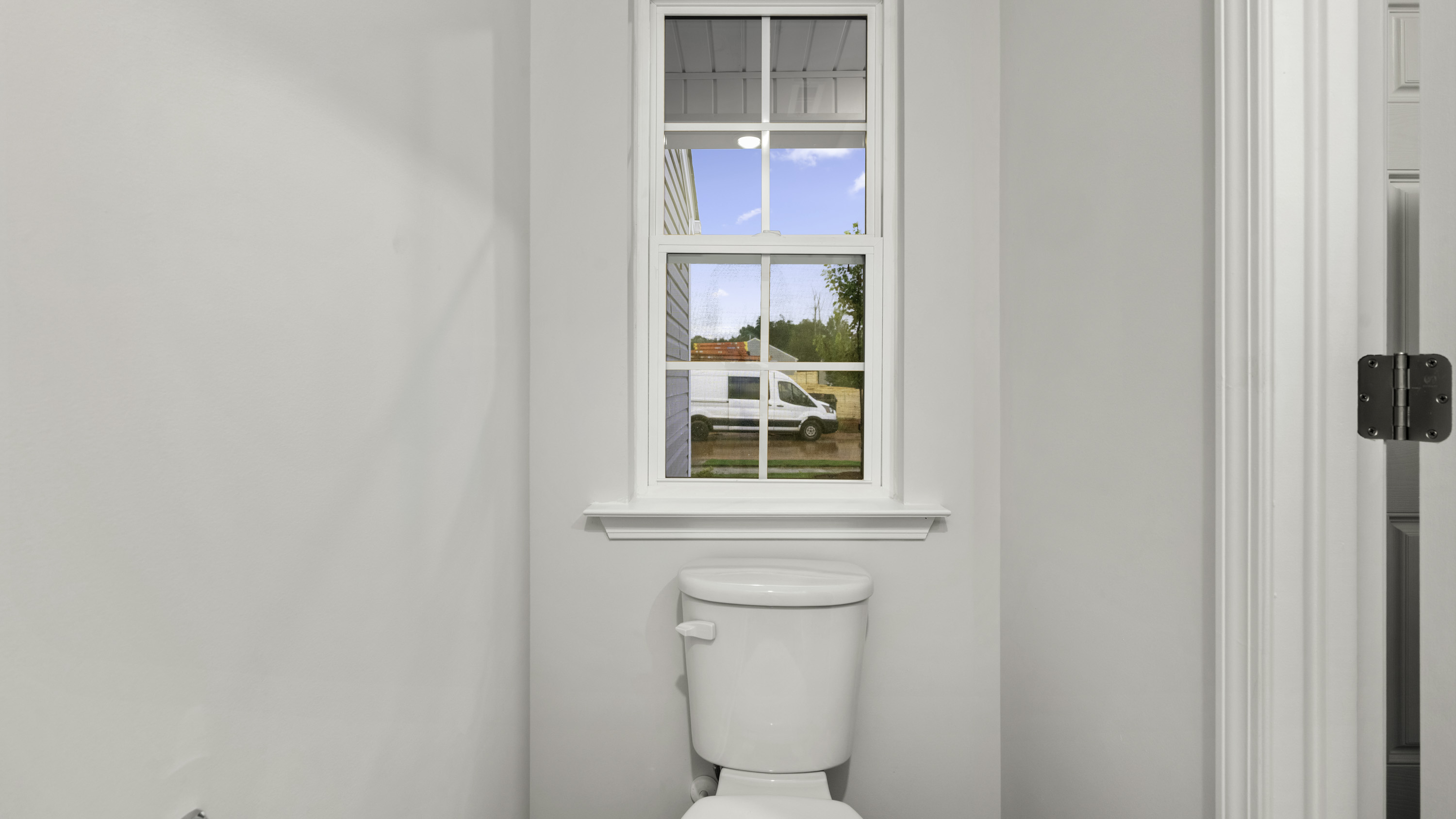 Double-hung, multi-pane window with a white sill and apron, paired with a white two-piece commode