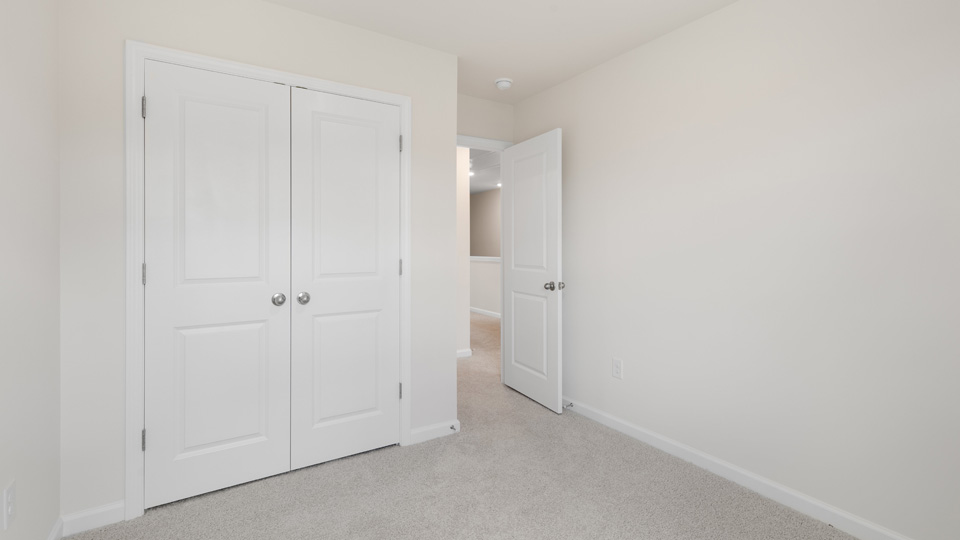 Neutral-toned interior space featuring light-colored wall-to-wall carpeting, white two-panel closet doors with round brushed nickel knobs, and matching interior passage door