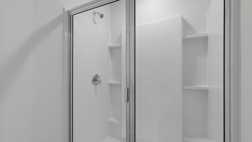 Walk-in shower enclosure with a hinged glass door, polished chrome fixtures, white wall surround, and integrated shelving