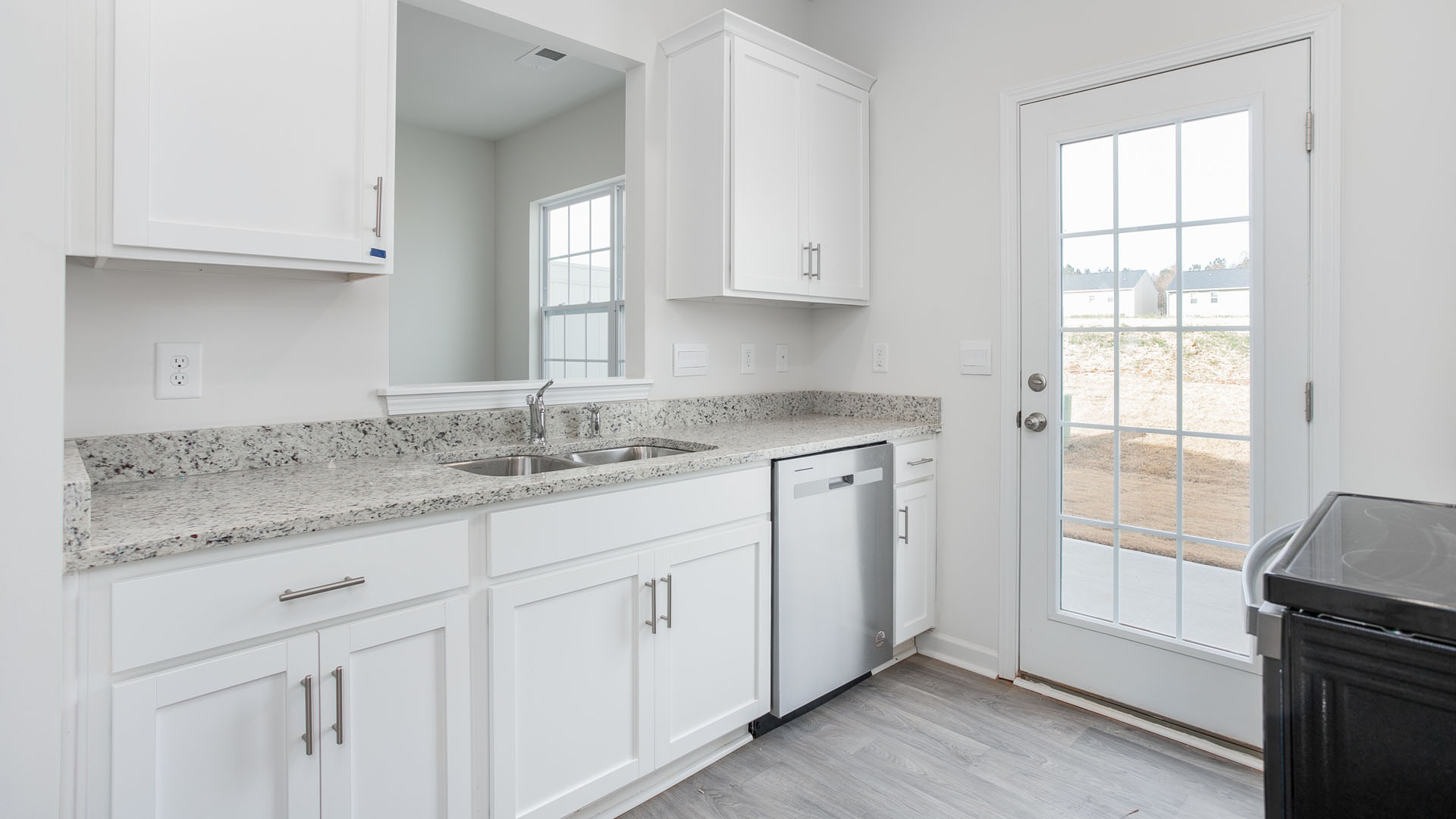 Kitchen featuring white shaker-style cabinetry, speckled stone countertops, a stainless steel dishwasher, wood-finish flooring, and a glass-paneled exterior door