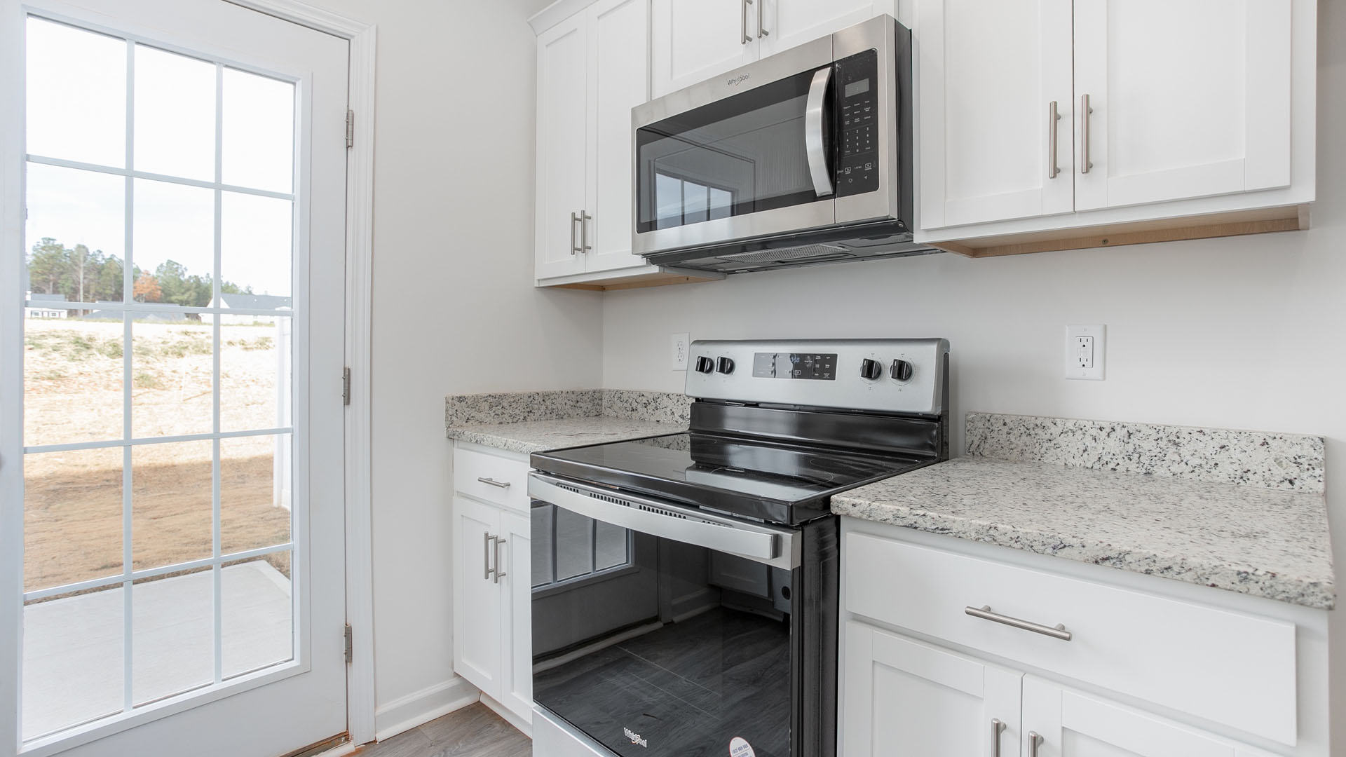 White cabinetry with silver-tone hardware, speckled stone-finish countertops, stainless steel microwave, black electric range, and glass-paned exterior door