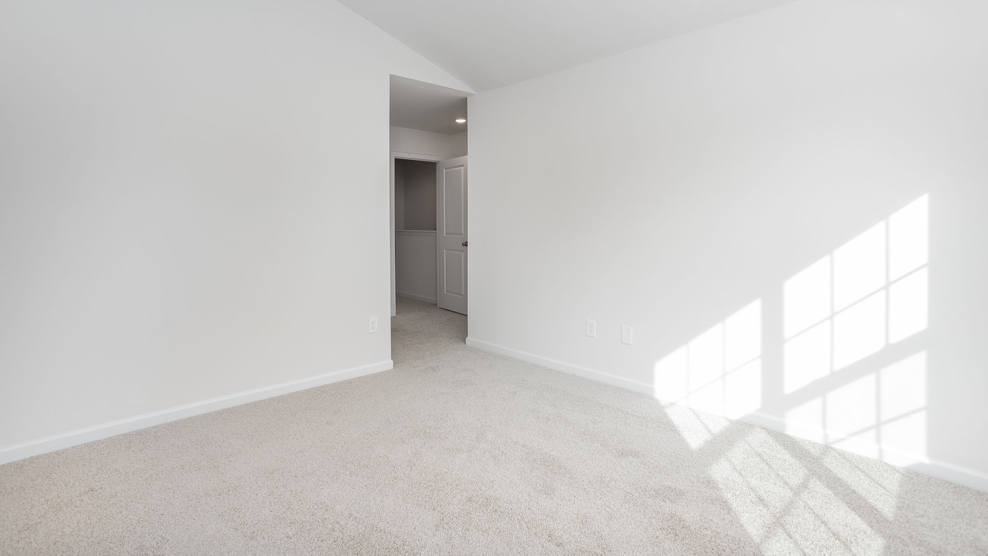 Neutral-toned carpeted flooring, vaulted ceilings, and a multi-pane window