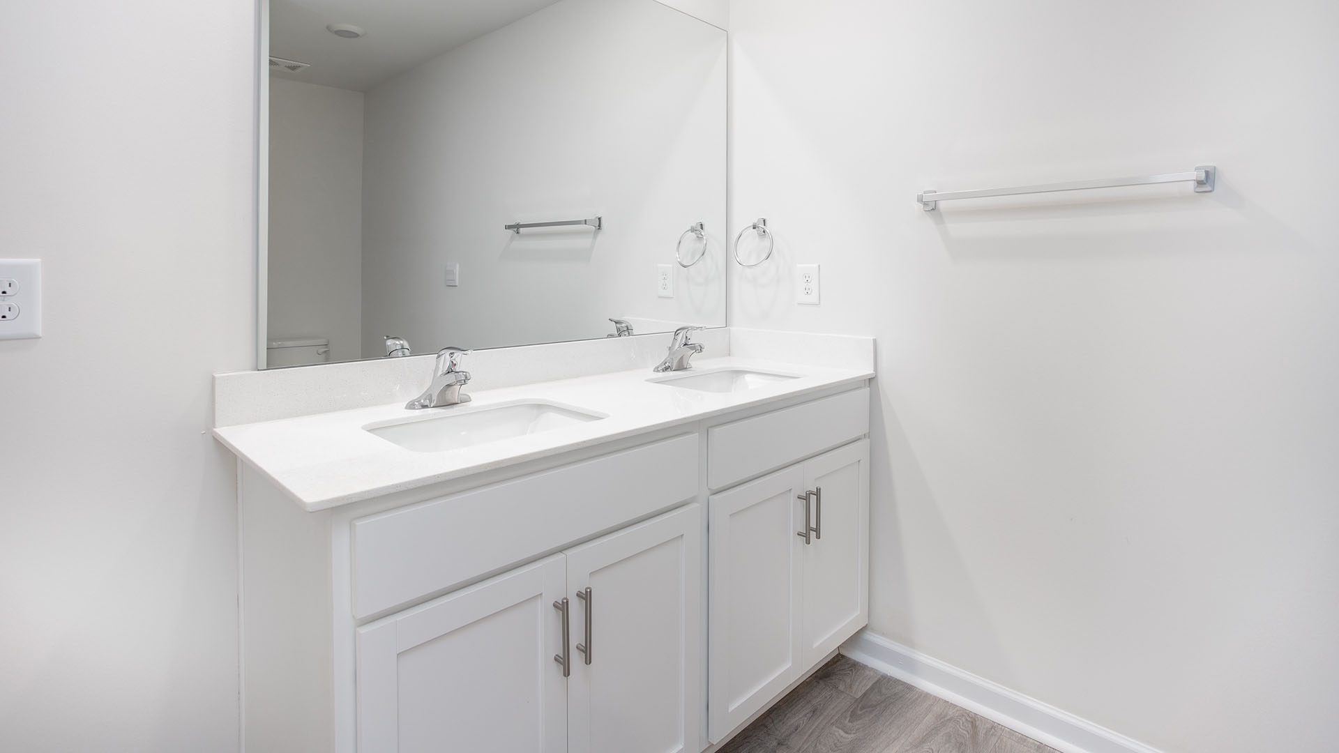 Double vanity featuring a white cabinetry base, rectangular undermount sinks, stone-finish countertops, chrome-finish faucets, and a full-width wall mirror