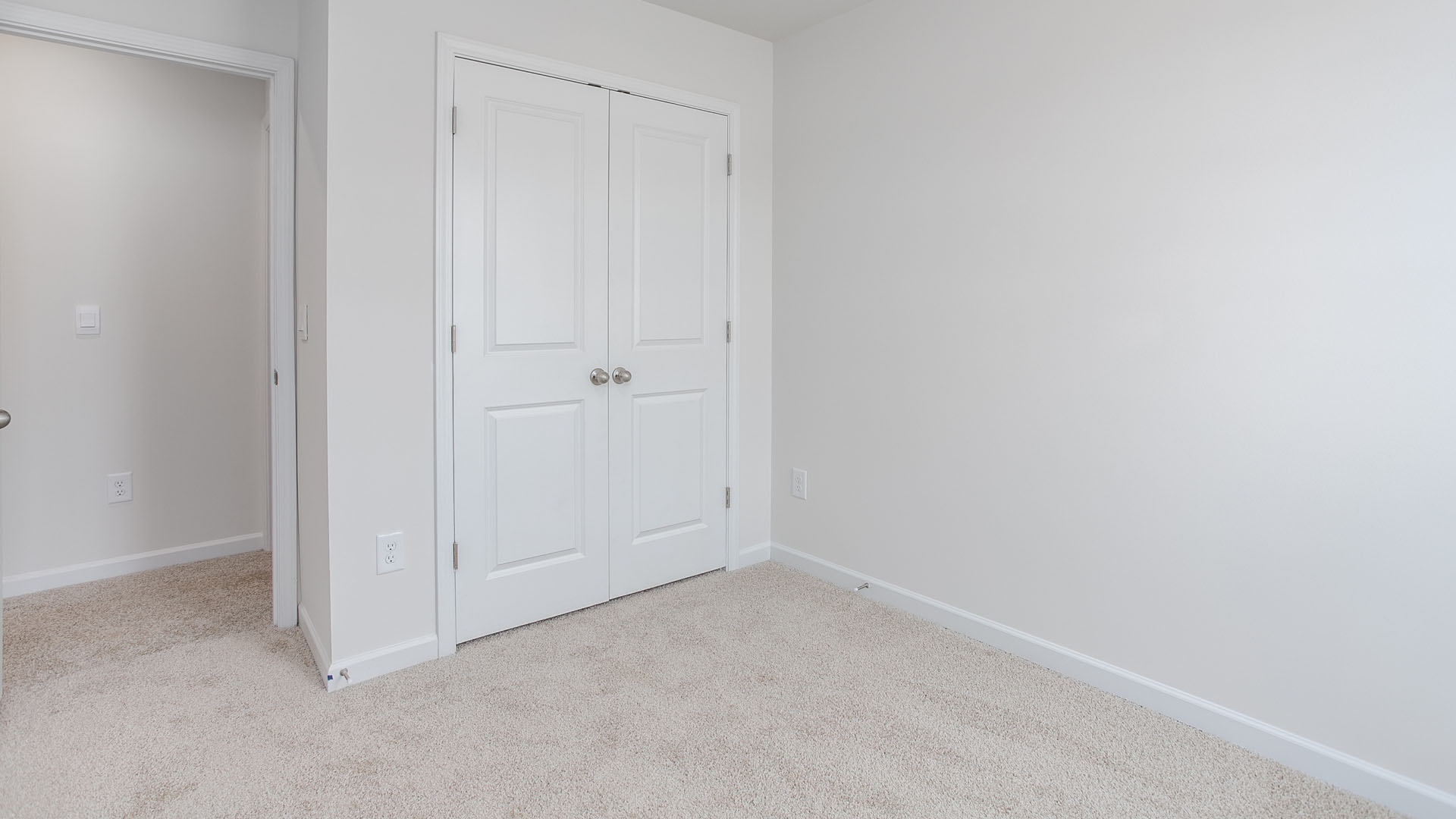 Neutral-toned wall-to-wall carpeting and double-panel closet doors with metallic hardware