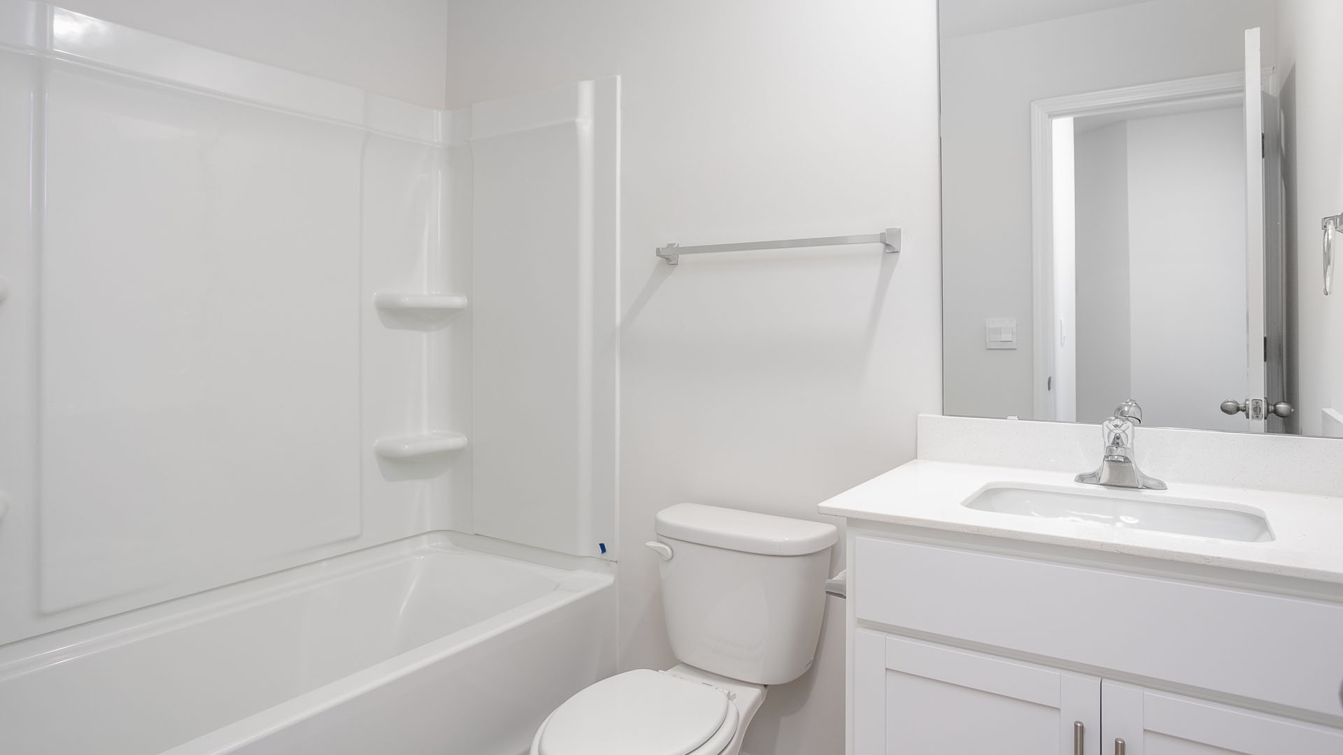 Bathroom featuring a white vanity cabinet with a solid surface countertop, an integrated rectangular sink, a wall-mounted mirror, and a tub-shower combination with integrated shelving