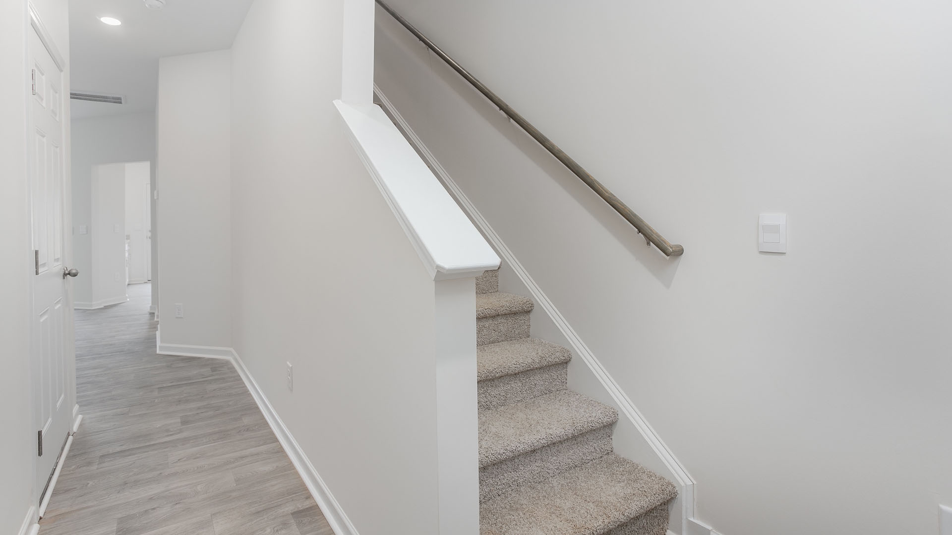 Staircase featuring wall-to-wall carpeting and a metal handrail, finished with wood-finish flooring in the hallway