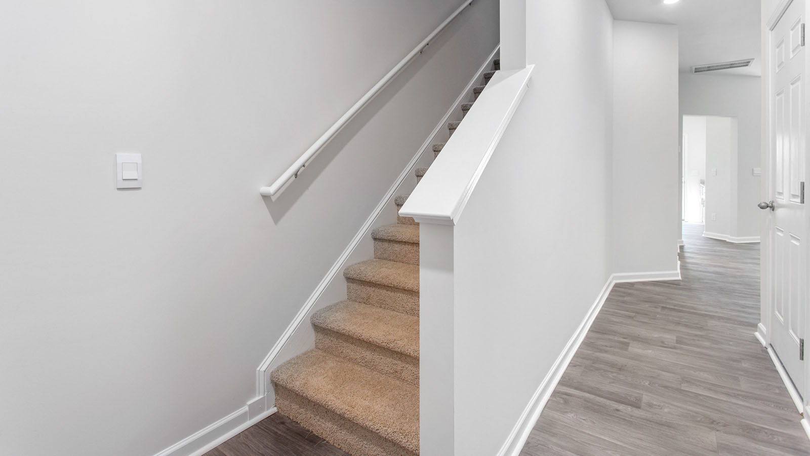 Staircase featuring neutral-toned carpeting, a white painted handrail, and wood-finish flooring