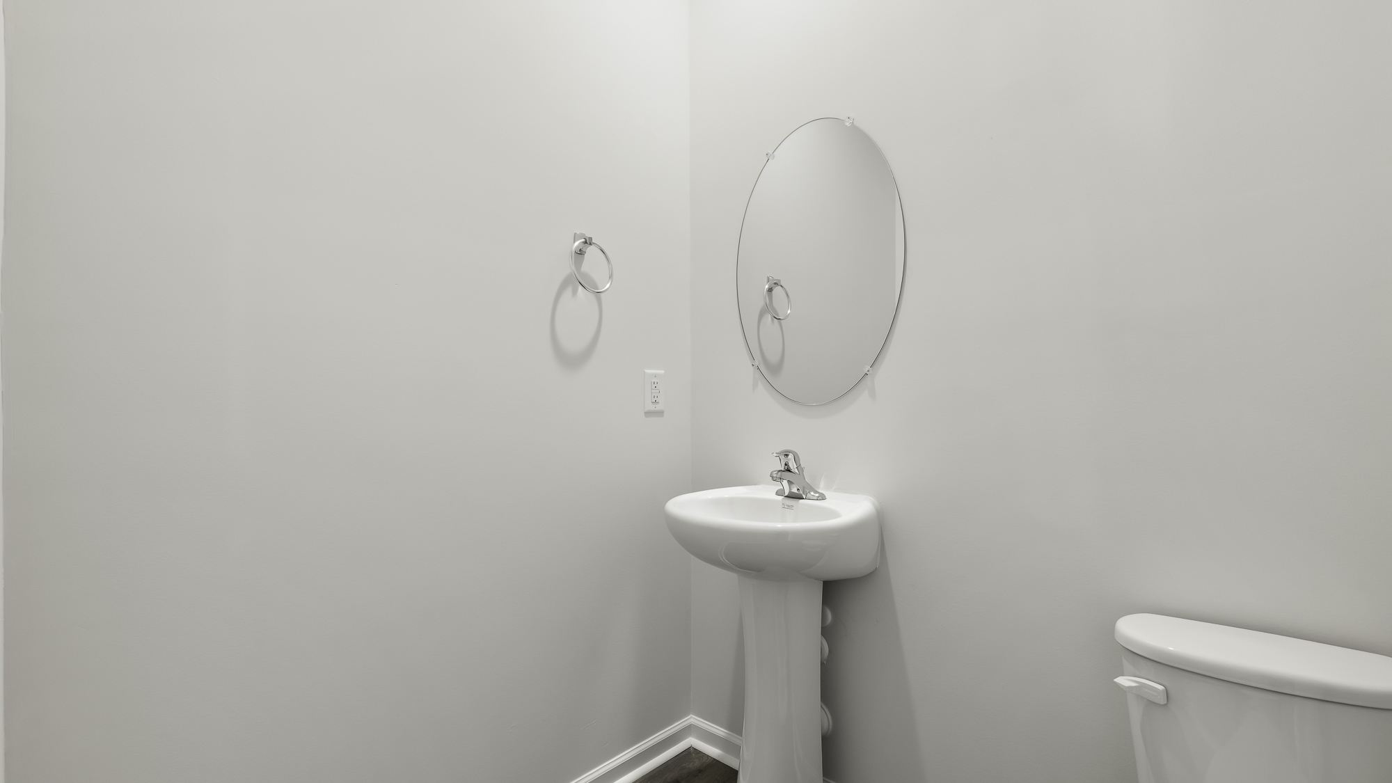 White pedestal sink with a chrome faucet, oval wall-mounted mirror, and wall-mounted metal towel ring