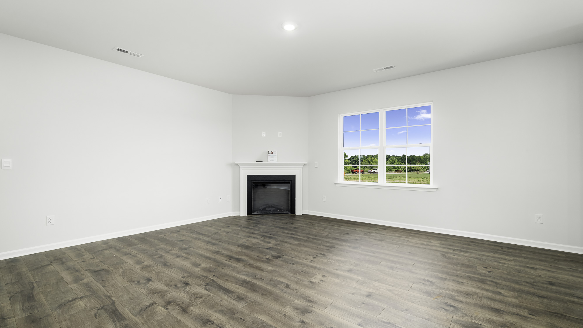 Interior room featuring wood-finish flooring, a corner fireplace with a white mantel, and multi-pane windows