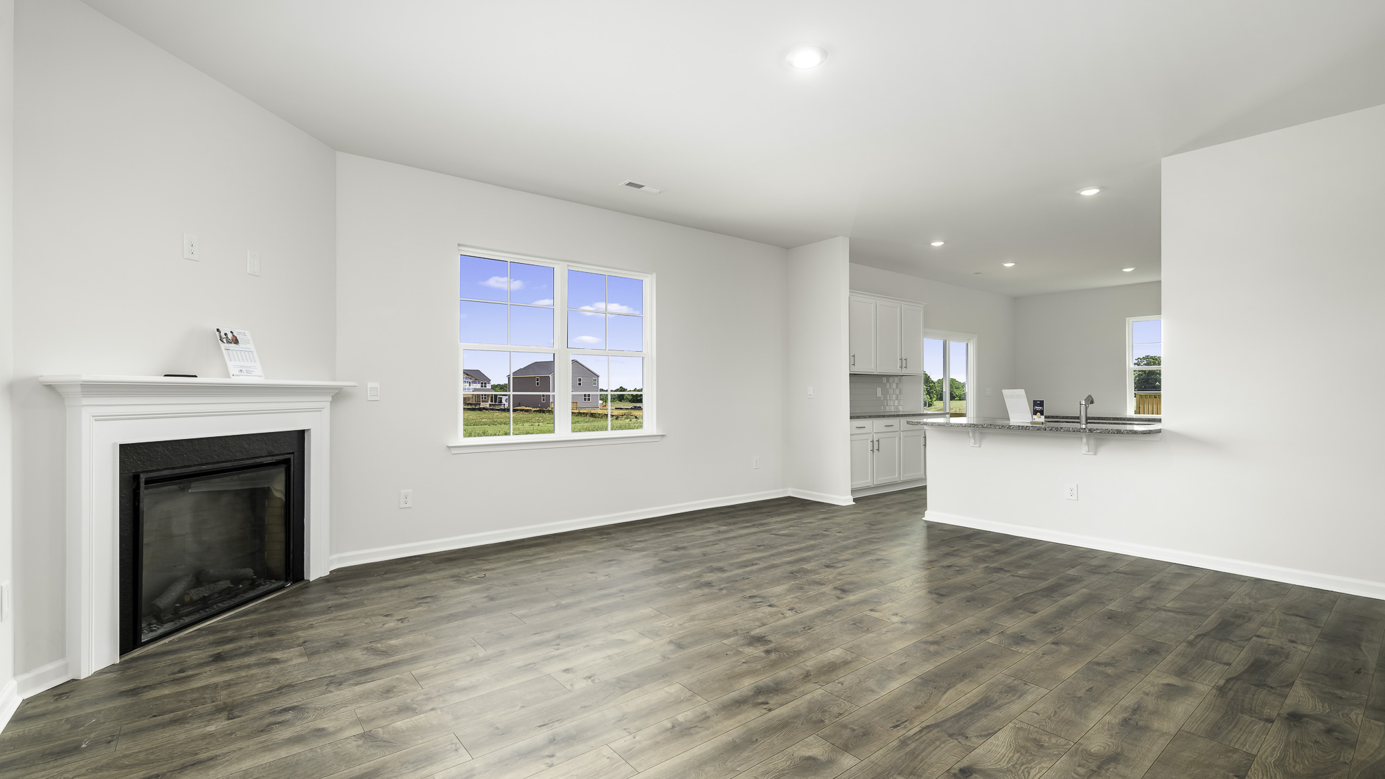 Living area featuring wood-finish flooring, a fireplace with a decorative mantel, multiple windows, recessed lighting, and a kitchen breakfast bar