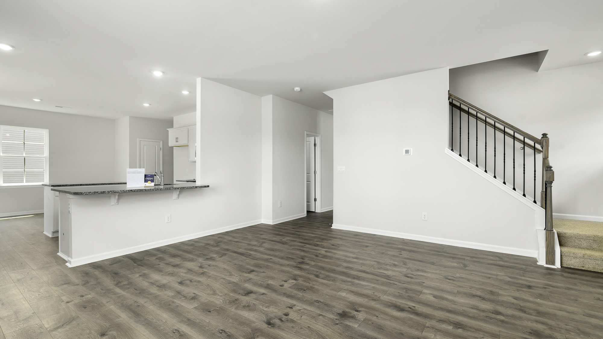 Open interior featuring wood-finish flooring, recessed lighting, a kitchen peninsula with stone-finish countertops, and a staircase with iron balusters