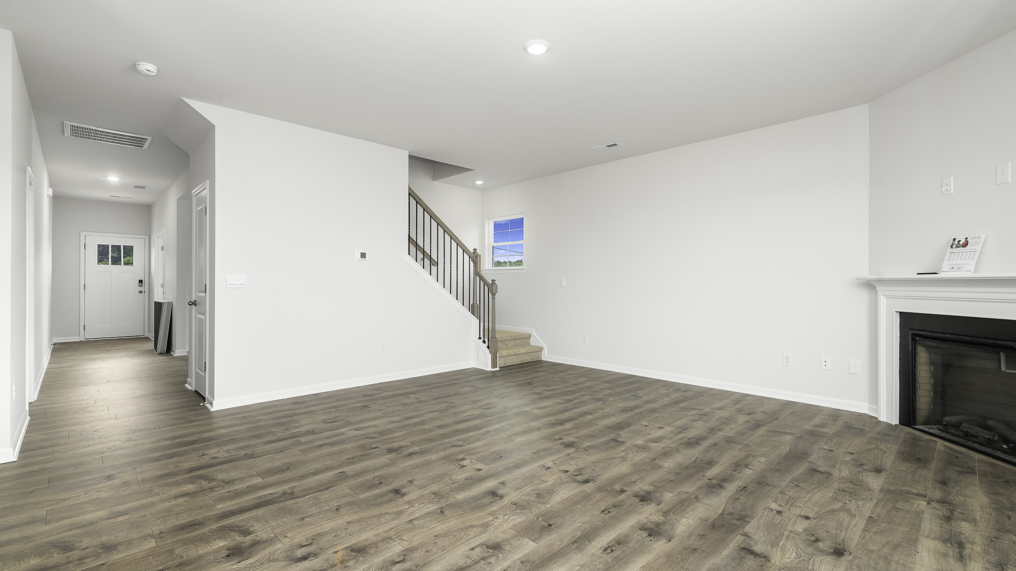 Open-concept interior featuring wood-finish flooring, a built-in fireplace with a mantel, recessed lighting, and a staircase with a wooden balustrade