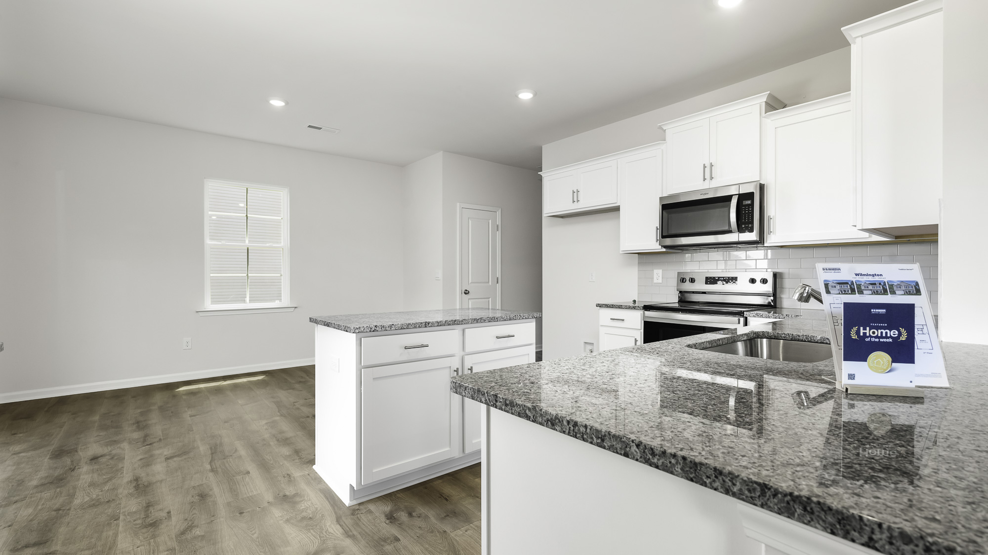 Kitchen featuring white shaker-style cabinetry, stone-surface countertops, a center island, stainless steel appliances, and wood-finish flooring