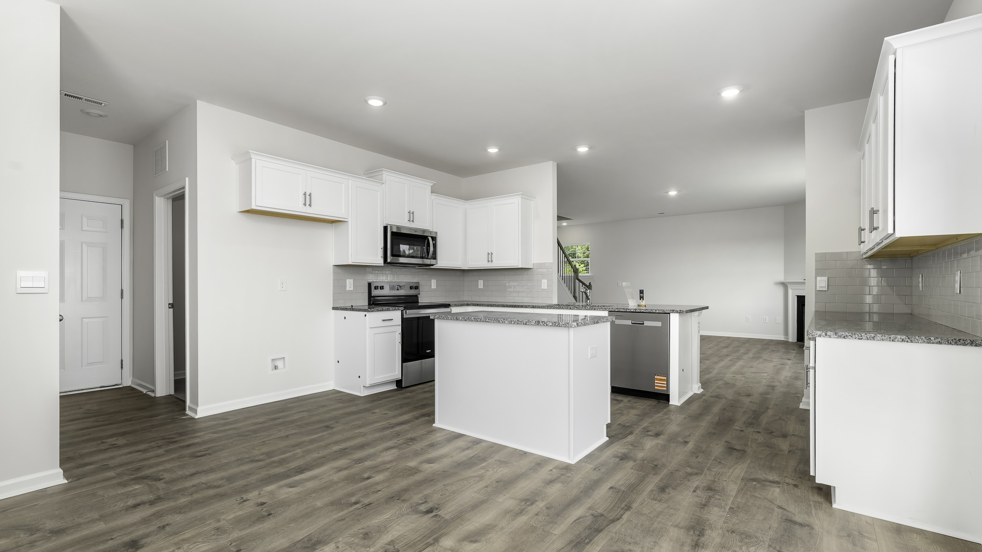 Kitchen featuring white shaker-style cabinetry, stone-finish countertops, stainless steel appliances, a center island, and wood-finish flooring