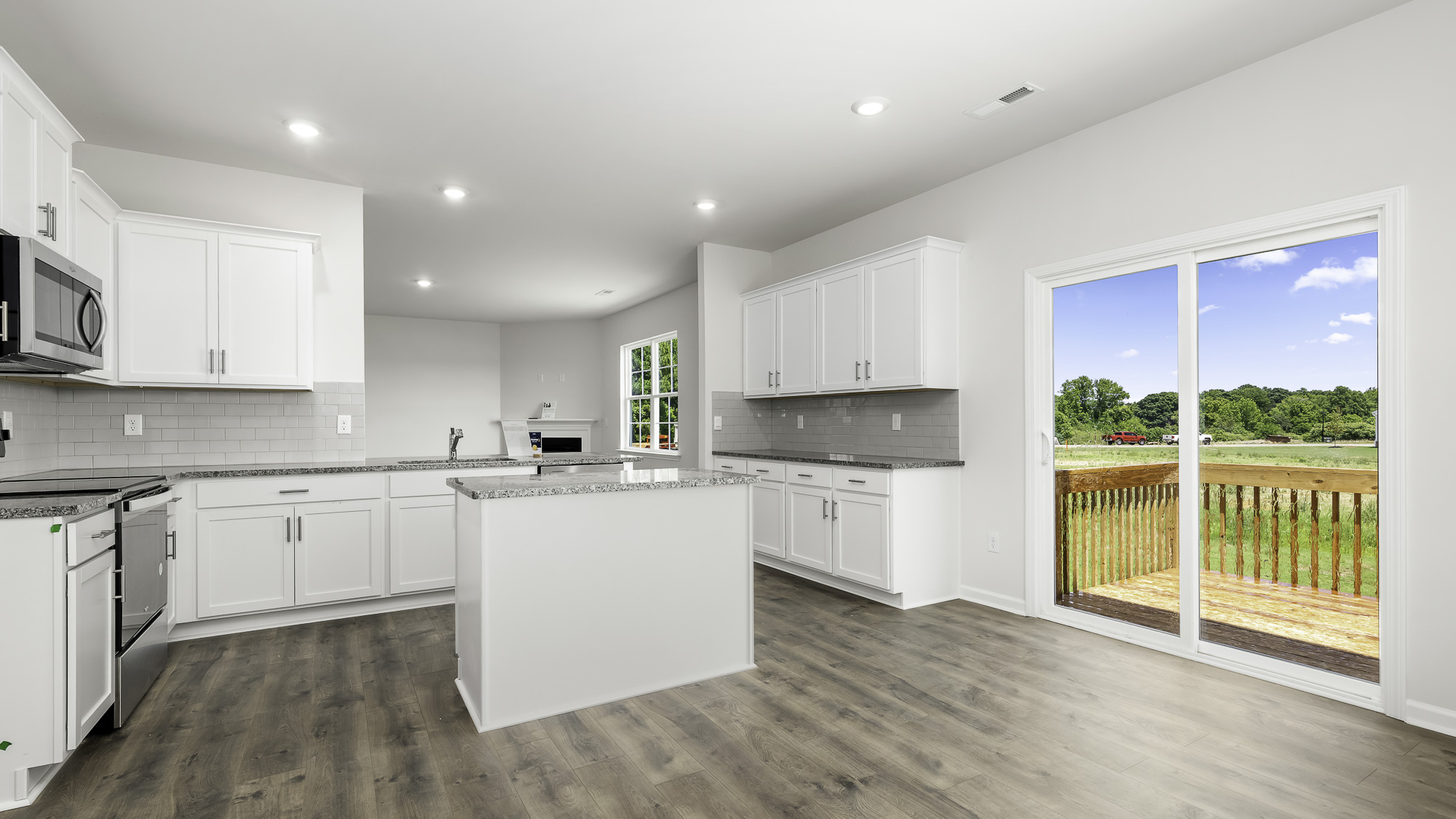 Kitchen featuring white cabinetry, stone-finish countertops, a central island, subway tile backsplash, and sliding glass doors with access to an exterior deck
