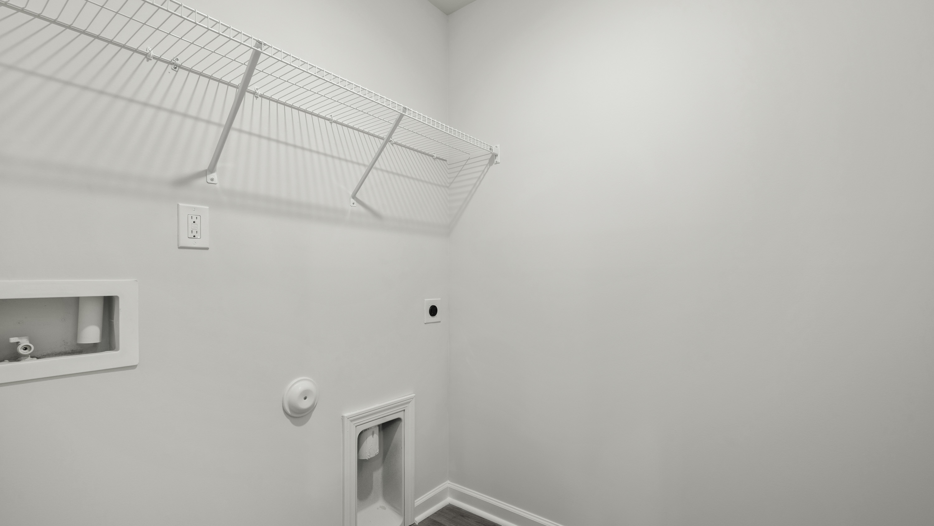 Utility area featuring white walls, a mounted wire shelf, dedicated plumbing connections for laundry appliances, and electrical outlets