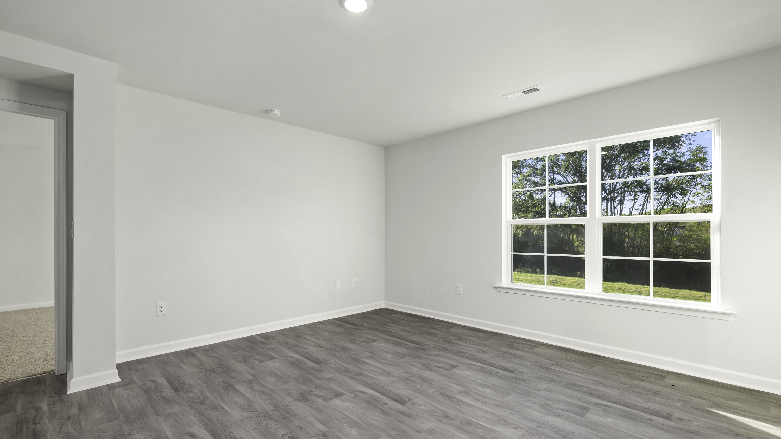 Neutral-toned interior space featuring wood-finish flooring, crisp white walls, and a multi-pane grid window