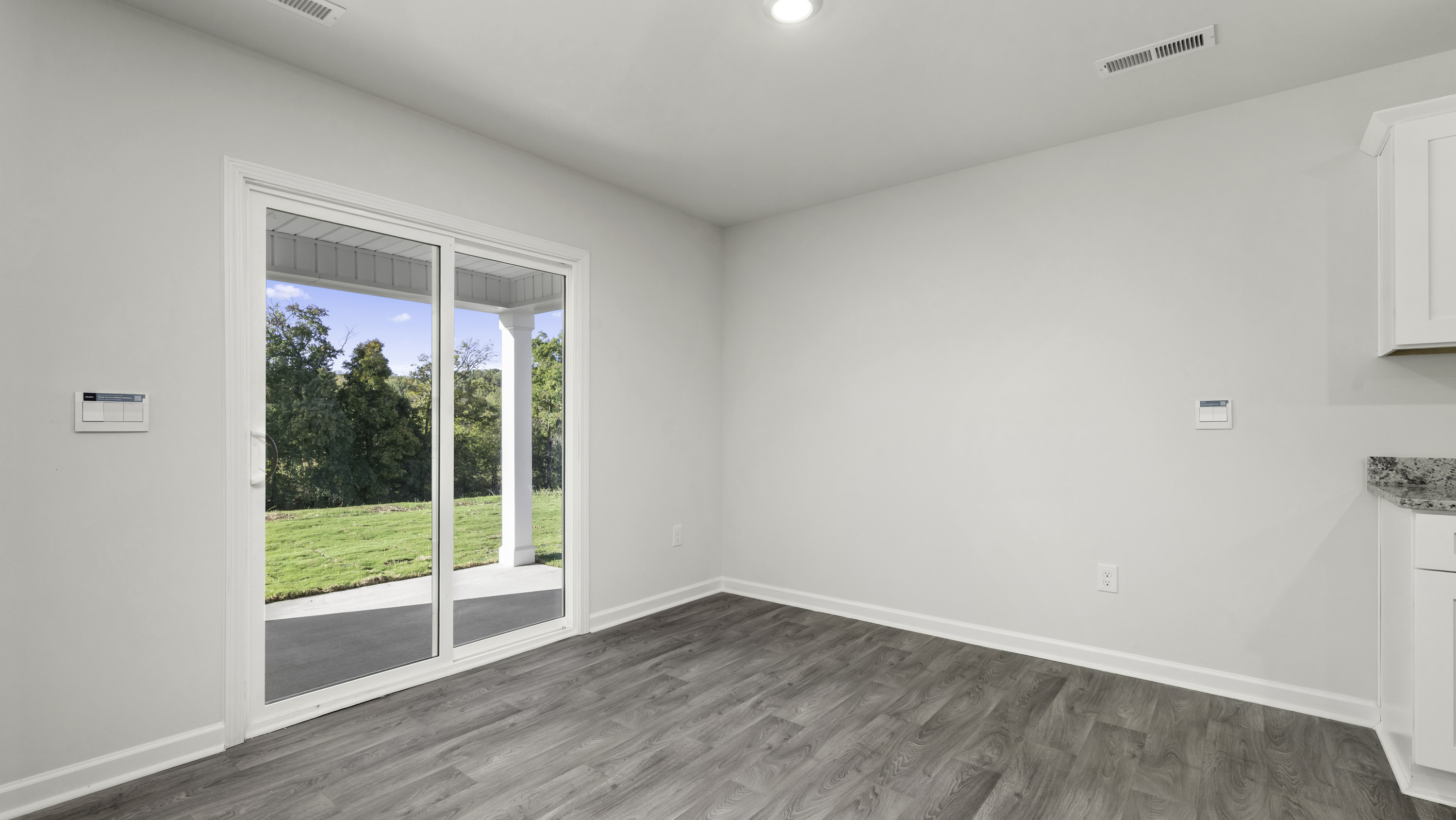 Sliding glass door opening to a covered patio, wood-finish flooring, recessed lighting, and white cabinetry with stone-surface countertops