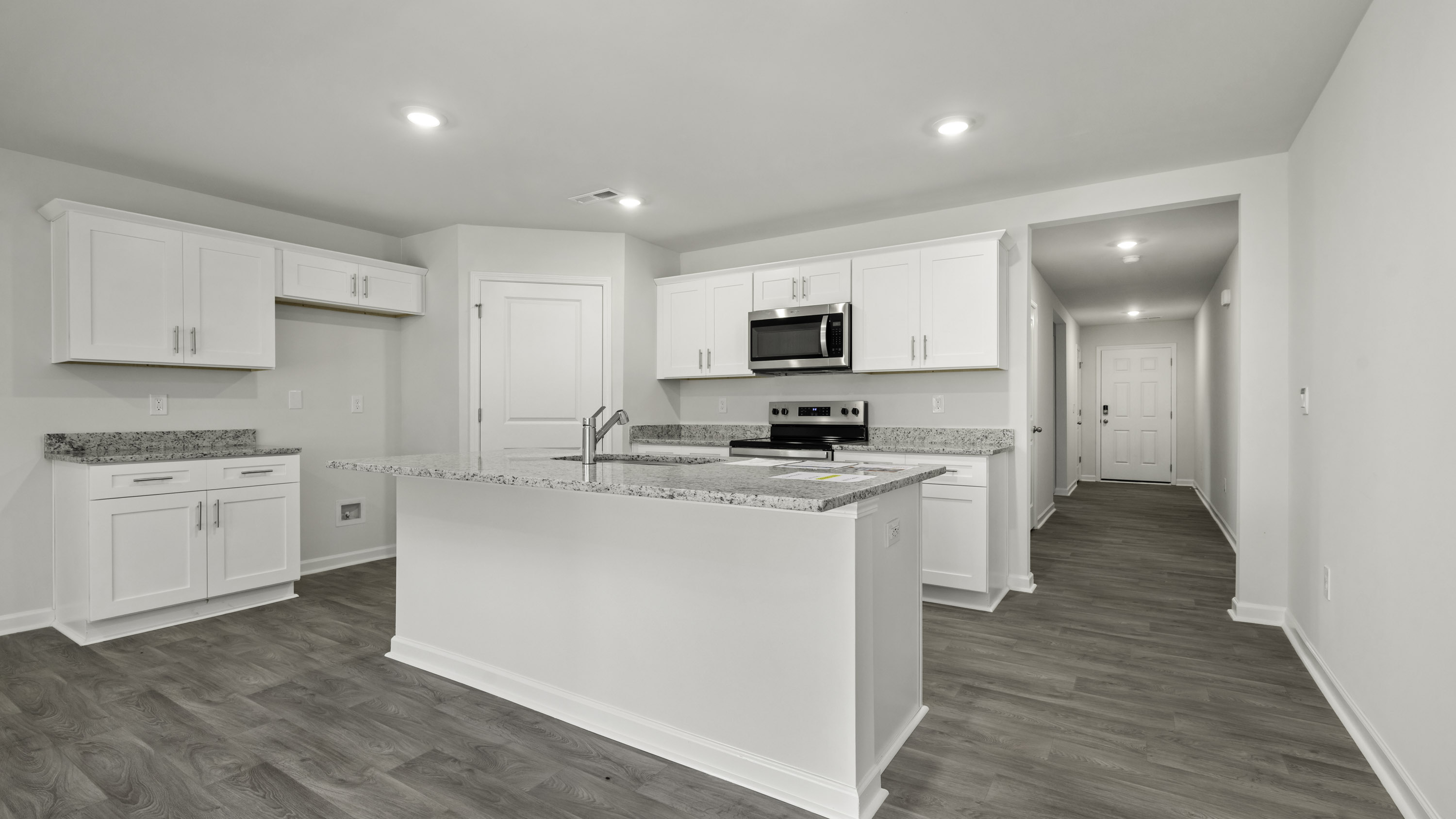 Kitchen featuring white cabinetry, a center island with a built-in sink, stone-finish countertops, stainless steel appliances, and wood-finish flooring