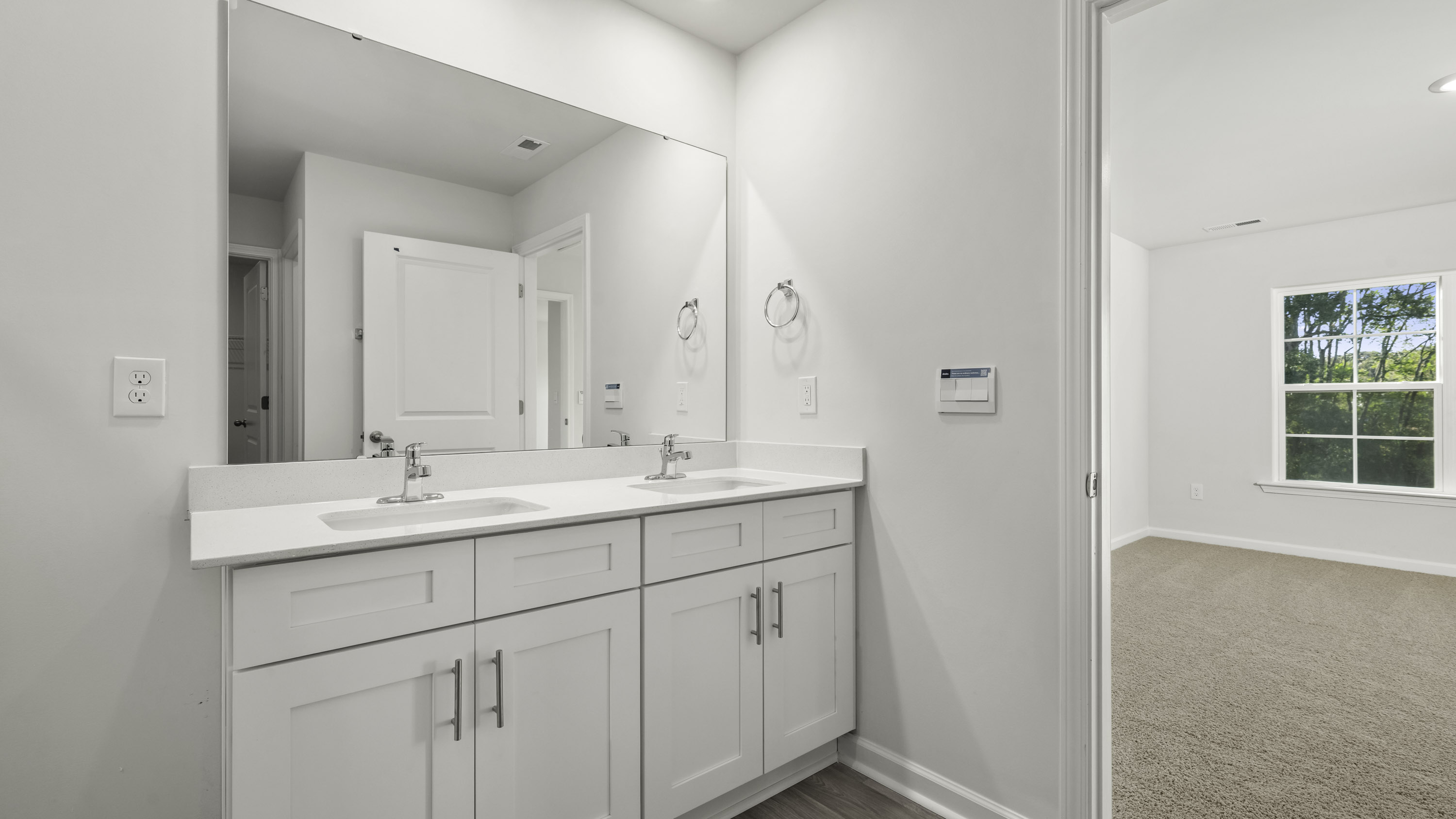 Double vanity with white cabinetry, rectangular under-mount sinks, solid-surface countertops, and a large frameless mirror